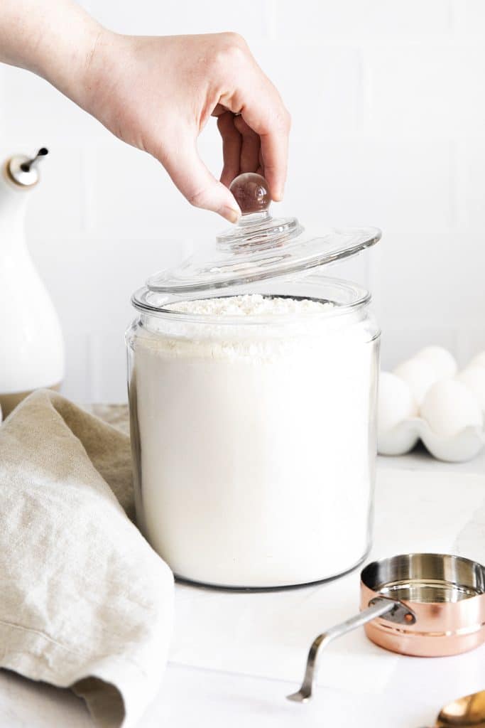 hand lifting a lid from a glass jar of flour.