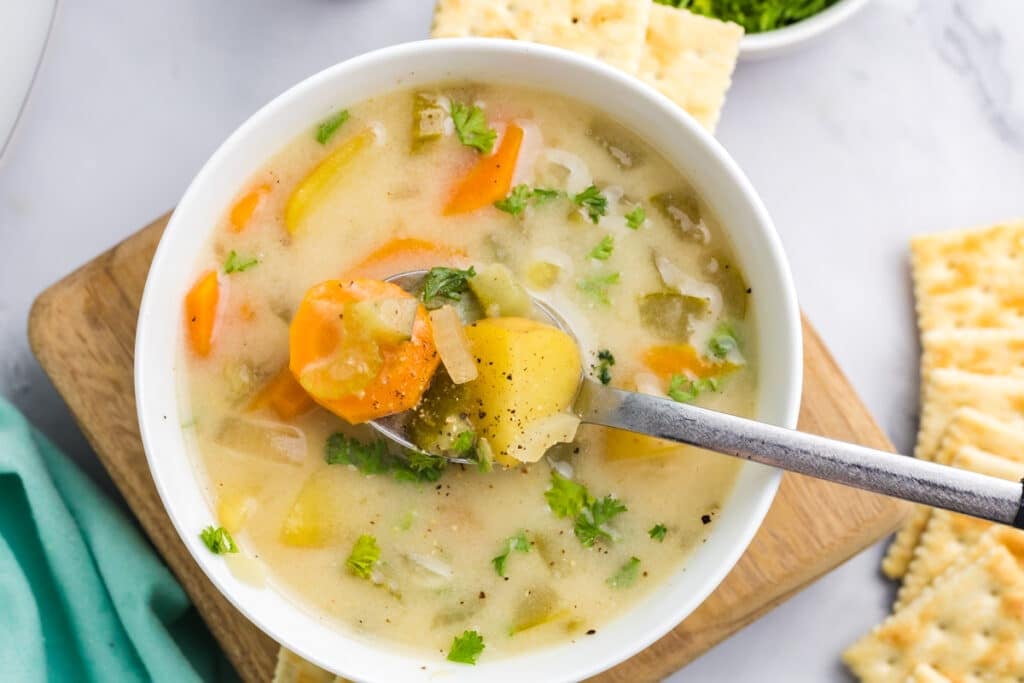 spoon with a bite of dill pickle soup in a bowl.