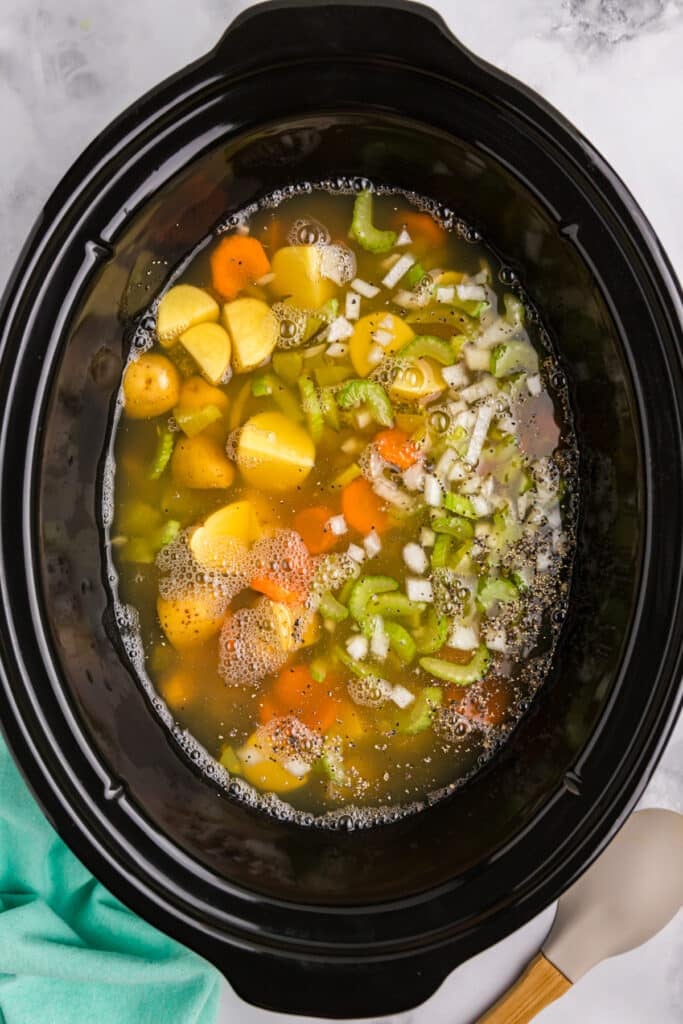 overhead shot of veggies and broth in a black slow cooker.