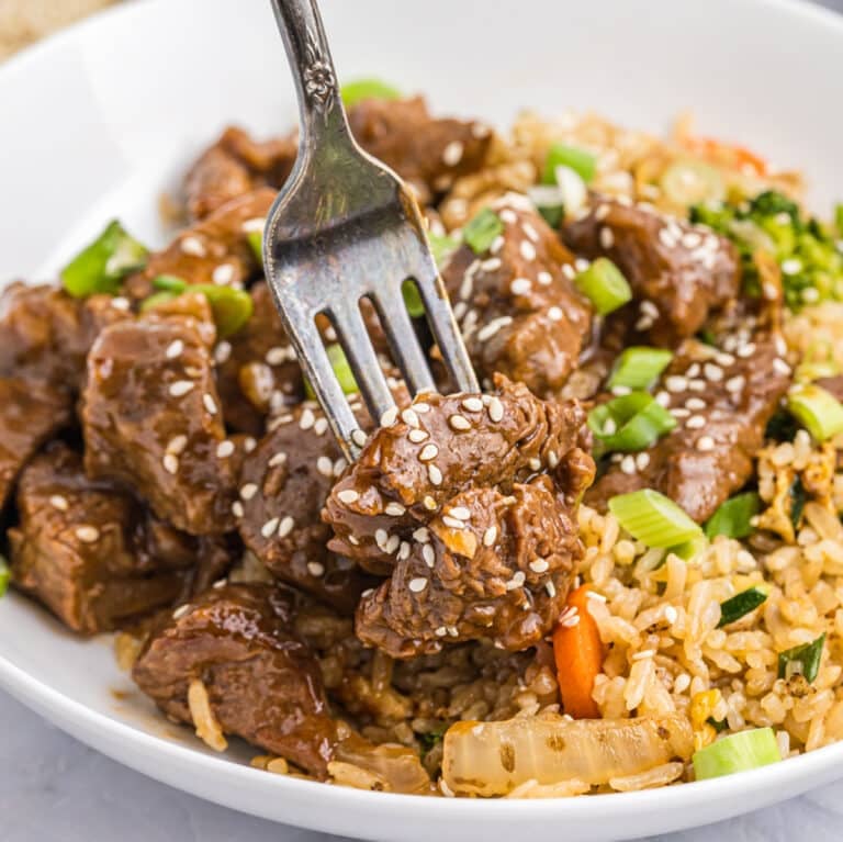 fork grabbing a bite of honey garlic steak bites on a plate with fried rice.