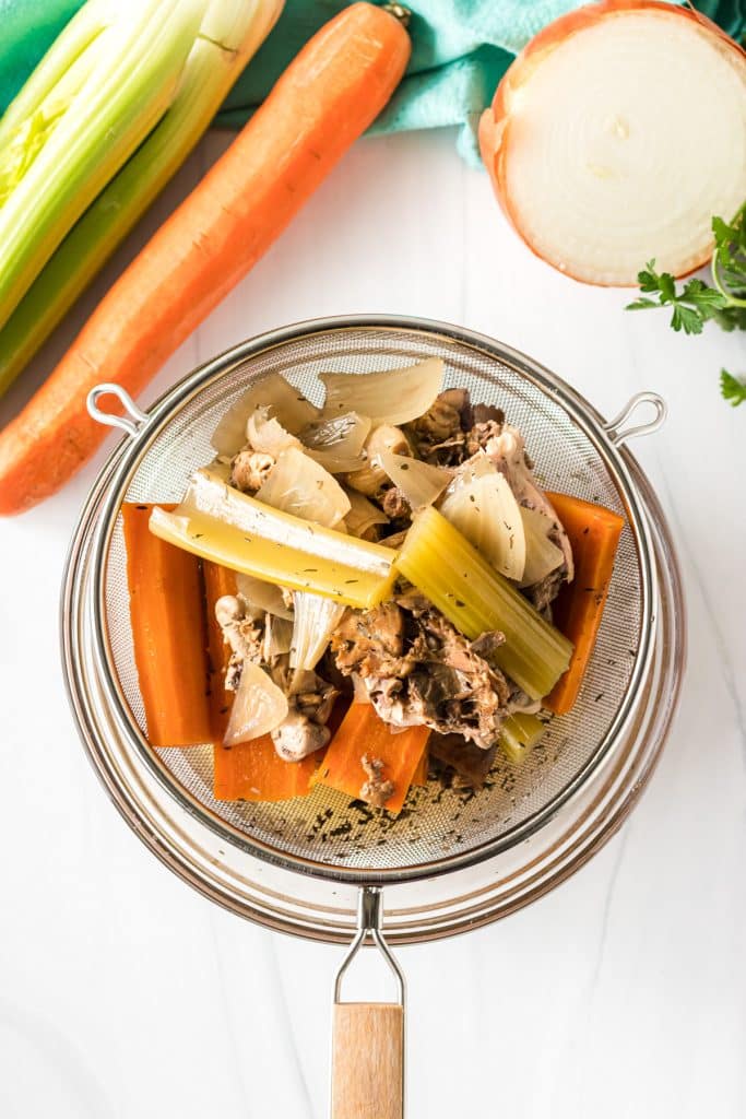 overhead shot of a strainer over a bowl making chicken stock.