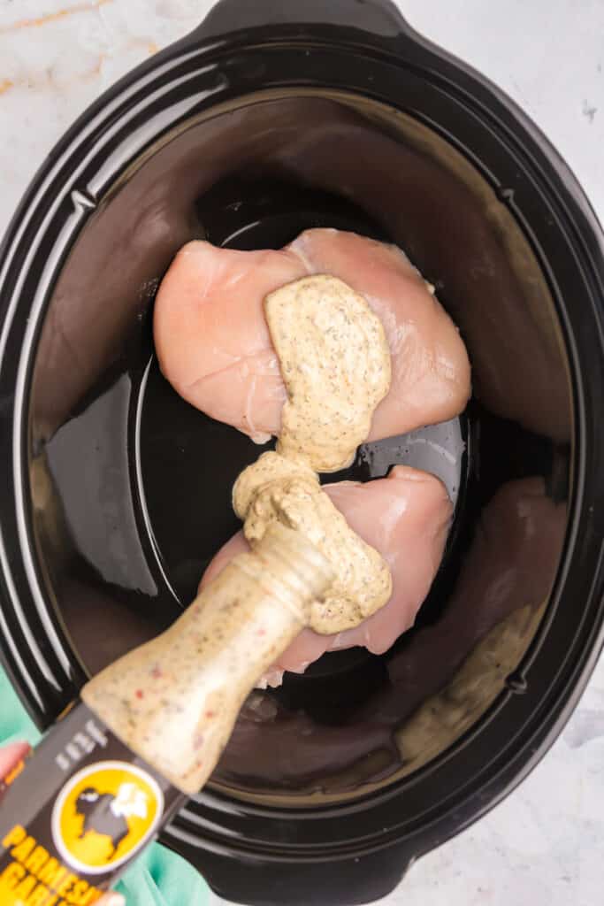 buffalo wild wings garlic parm sauce pouring into a crockpot with chicken breasts.