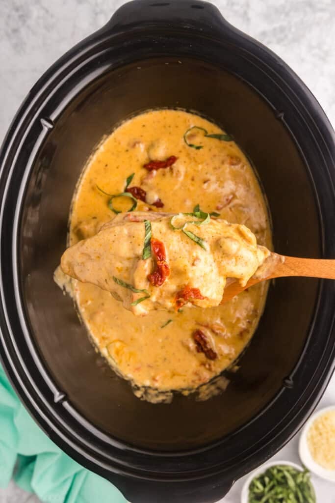 spoon lifting a marry me chicken breast from a slow cooker.