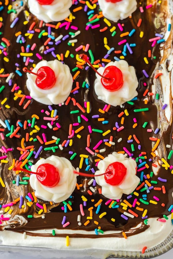 overhead shot of banana split lush in a pan topped with sprinkles, whipped cream, and cherries.