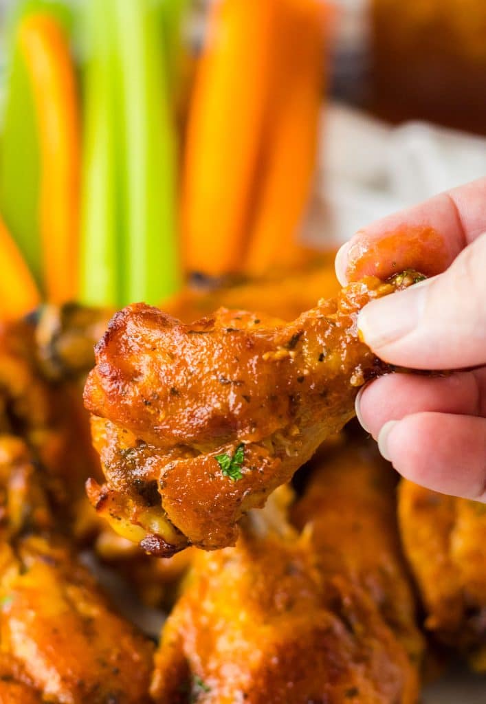 hand holding a chicken wing in front of sliced carrots & celery.