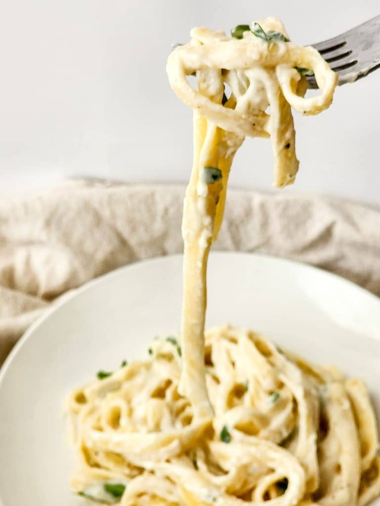 fork lifting a bite of alfredo pasta from a plate.