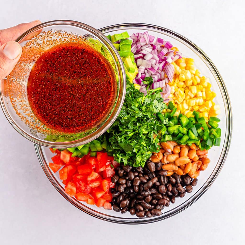 hand pouring a bowl of dressing into a bowl of vegetables.