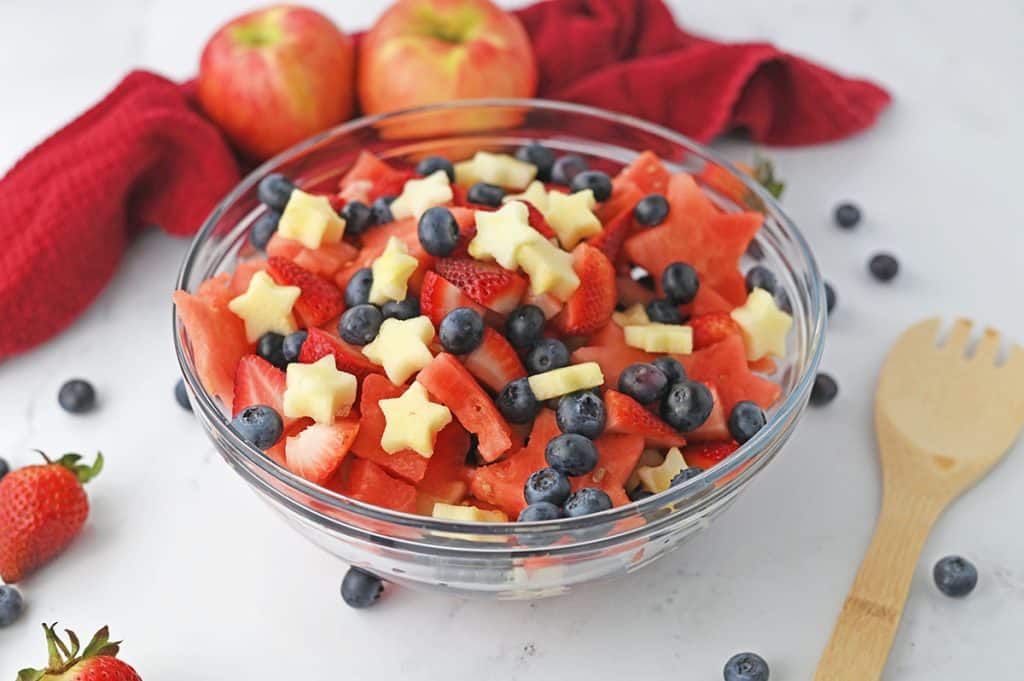 bowl of fruit salad next to a wooden spoon.