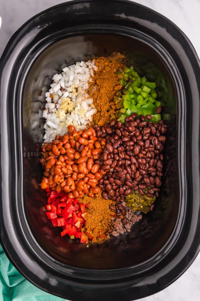 overhead shot of beans and diced veggies in a crockpot to make frito pie.