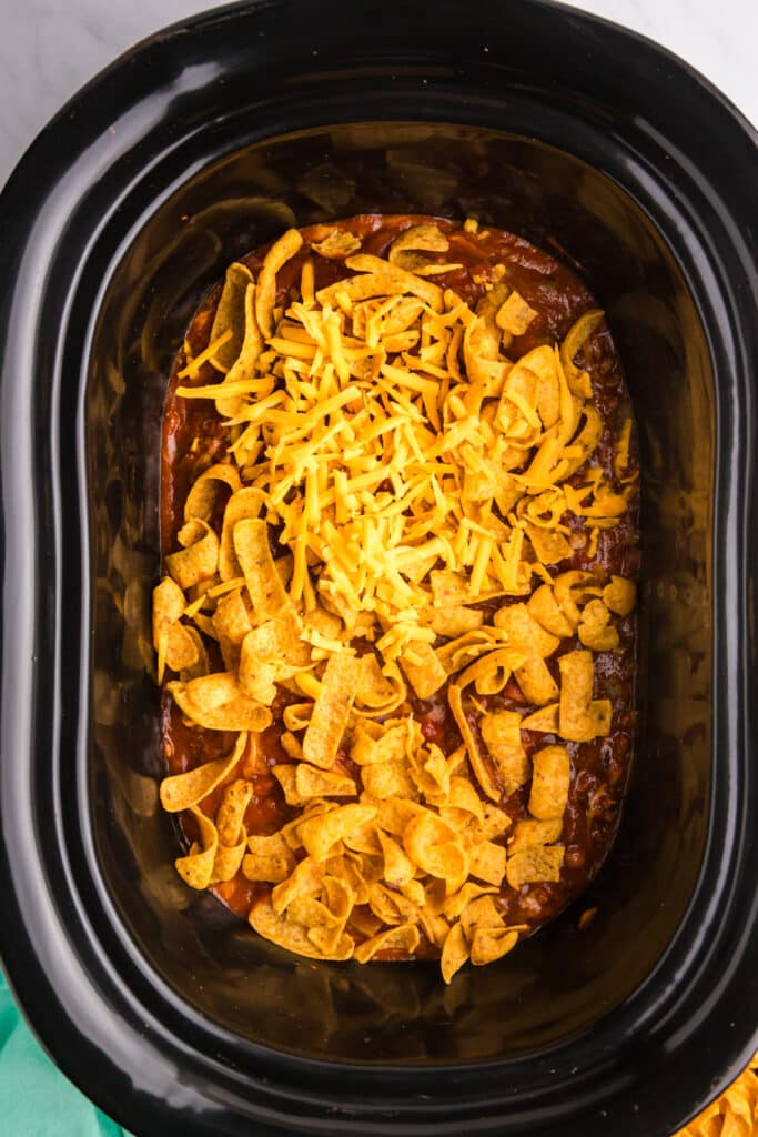 overhead shot of fritos and shredded cheddar in a crockpot.