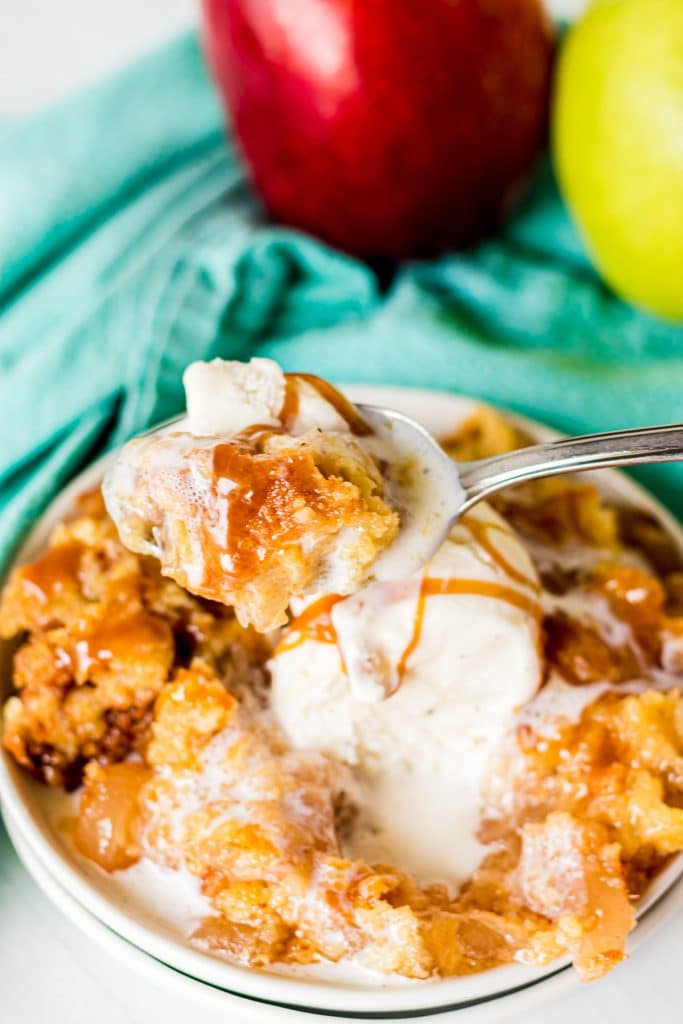 spoon lifting a bite of apple dump cake with vanilla ice cream.