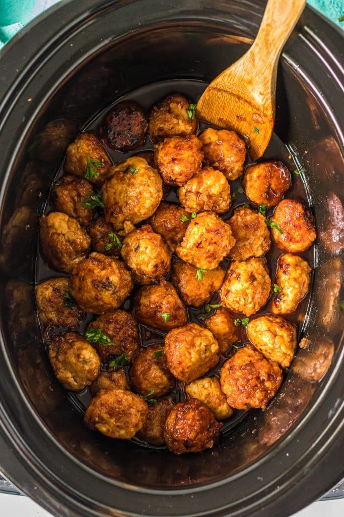 firecracker chicken meatballs in a slow cooker with a wood spoon.