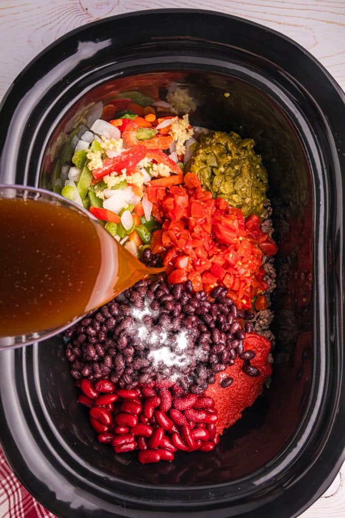 beef broth being poured into a slow cooker of chili.