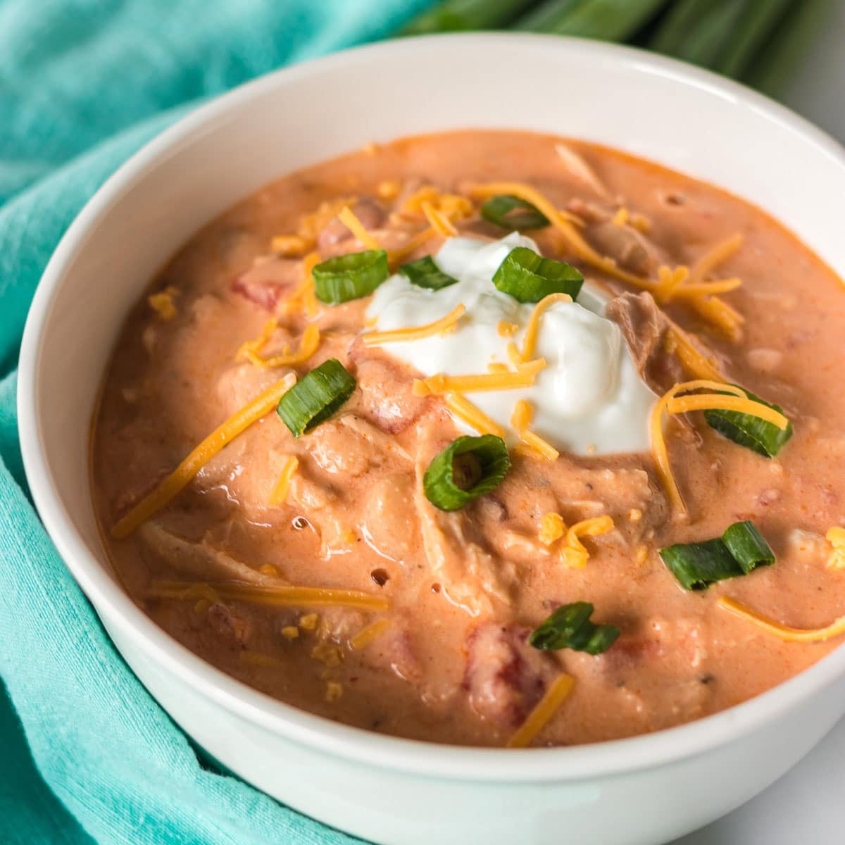 white bowl of buffalo chicken chili topped with sour cream, scallions, and shredded cheese.