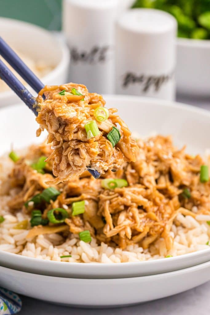 chopsticks lifting a bite of teriyaki chicken from a bowl.