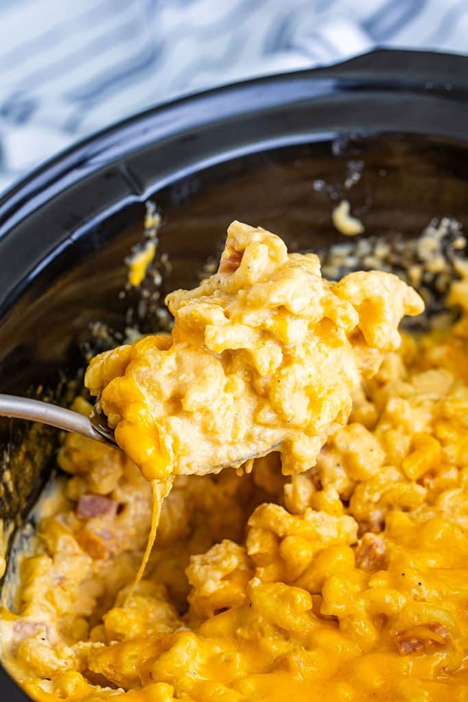 spoon lifting a scoop of mac and cheese with ham from a crockpot.