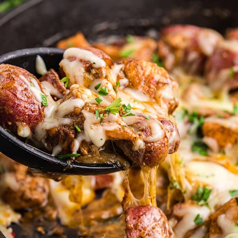spoon lifting a scoop of garlic parmesan chicken & potatoes from a skillet.