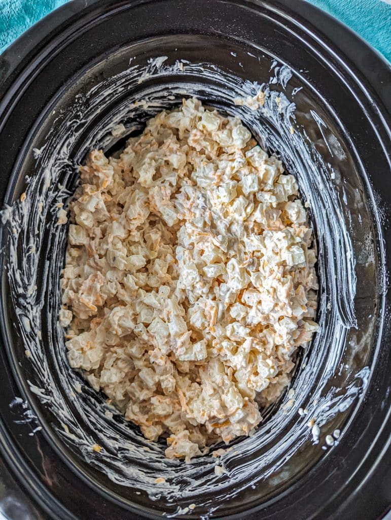 overhead shot of cheesy potatoes in a slow cooker before cooking.