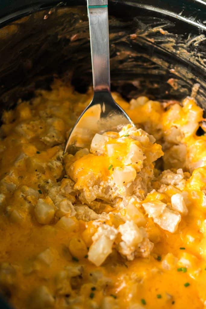 spoon lifting a scoop of cheesy potatoes from a crockpot.