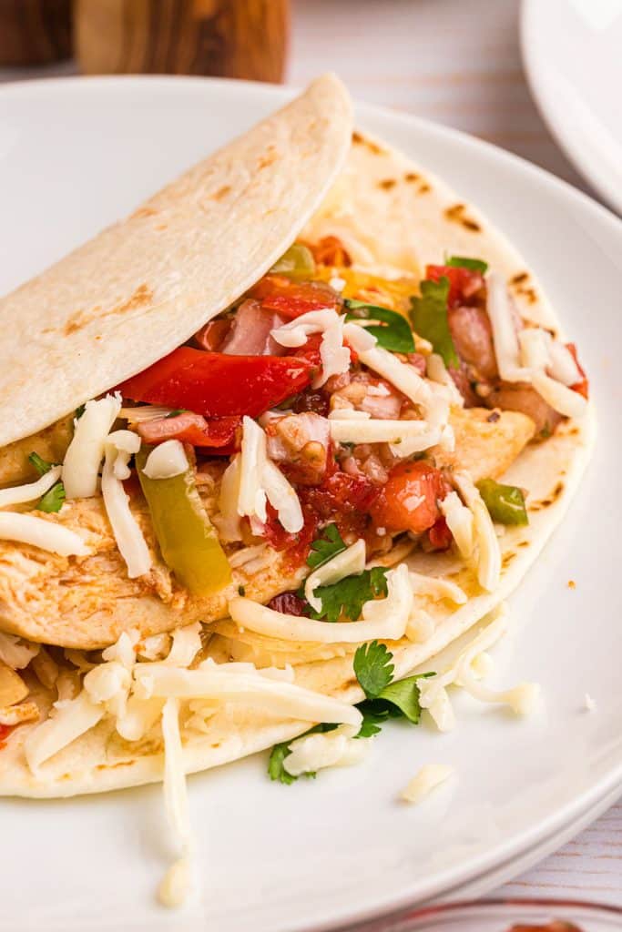 closeup of a chicken fajita on a white plate.