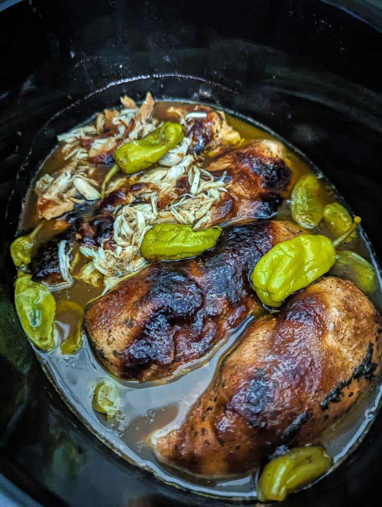 overhead shot of chicken breasts, pepperoncinis in a slow cooker.