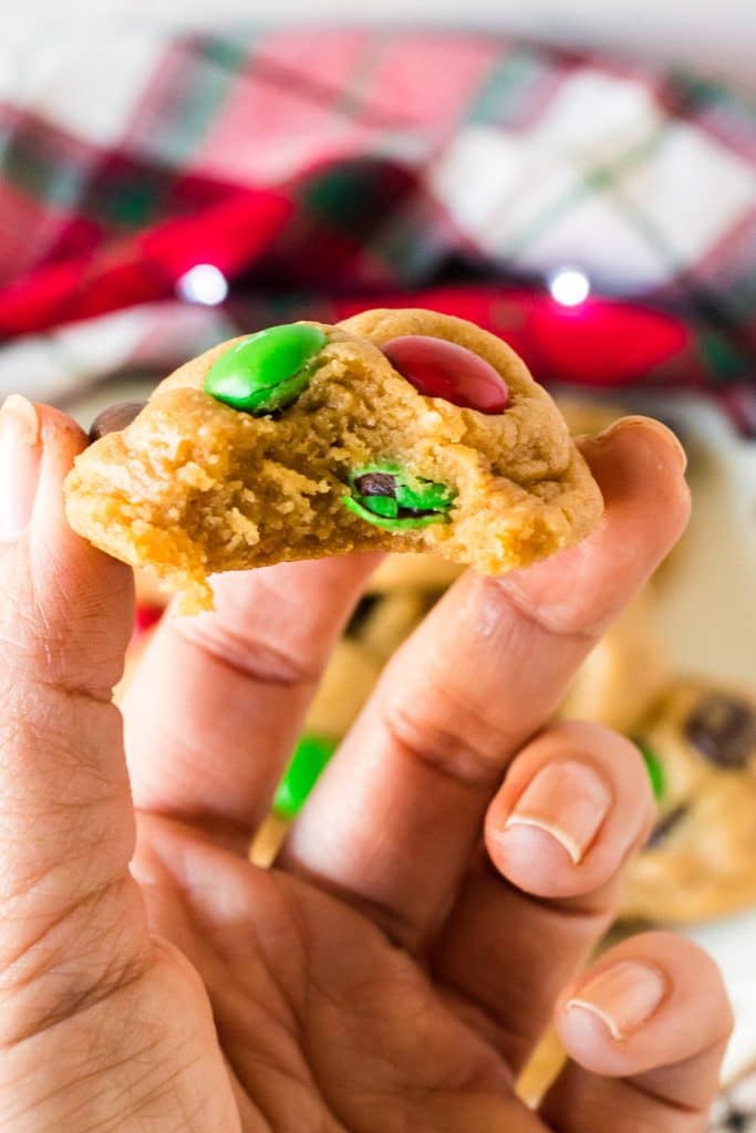 hand holding an M&M cookie with a bite missing.