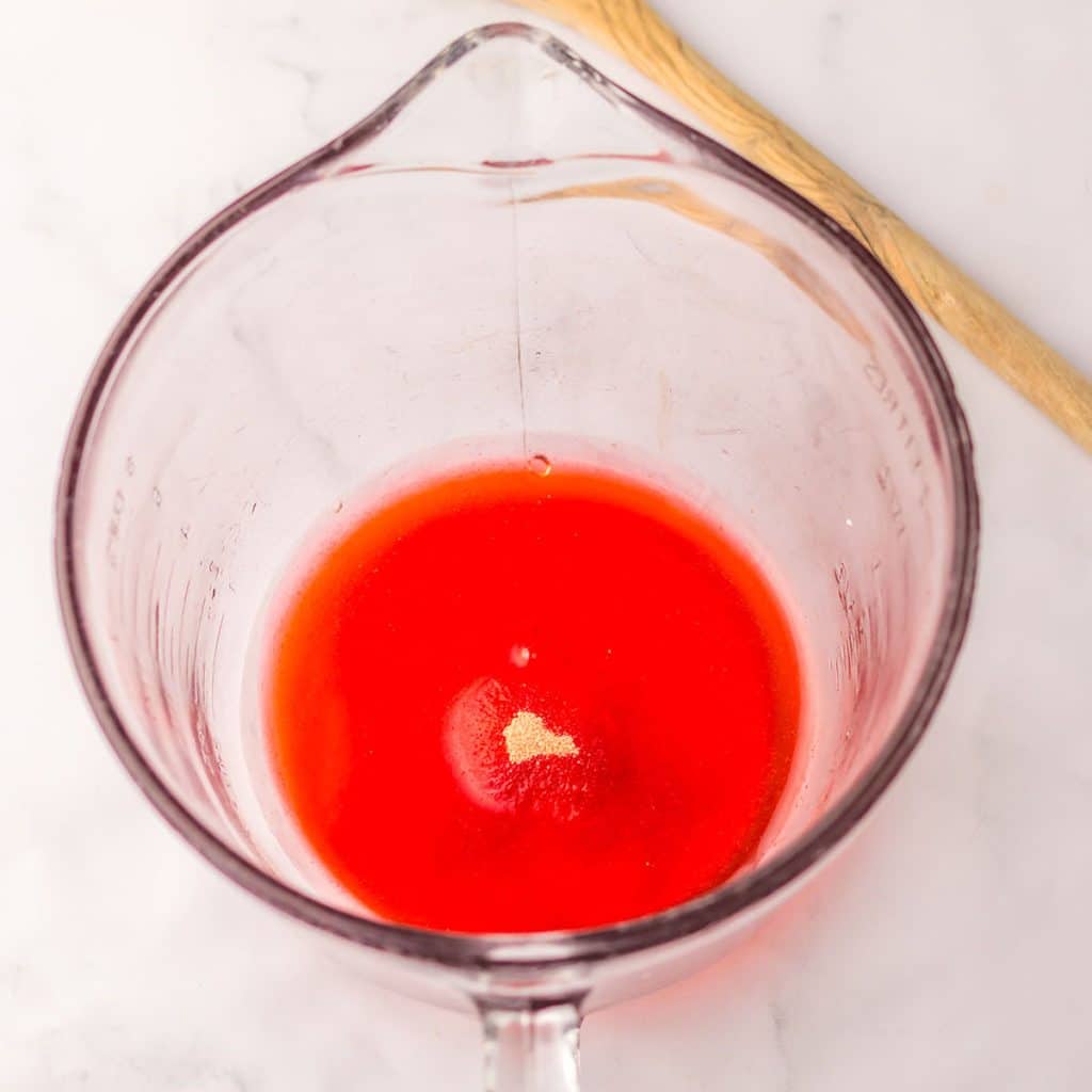 overhead shot of glass measuring cup with red liquid gelatin.