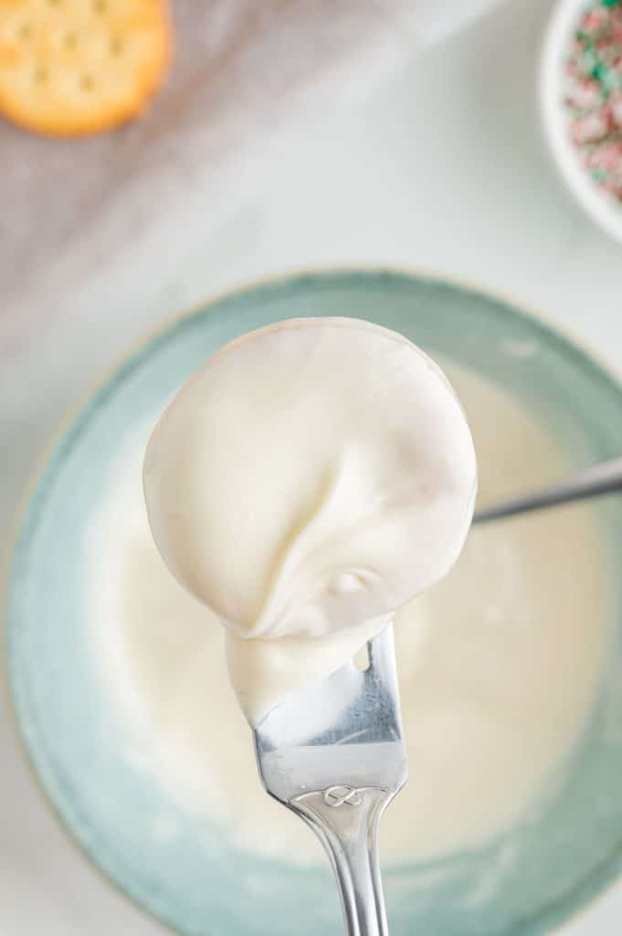 fork lifting a cookie from melted white chocolate.
