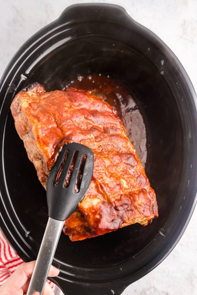 tongs lifting ribs from a crockpot.