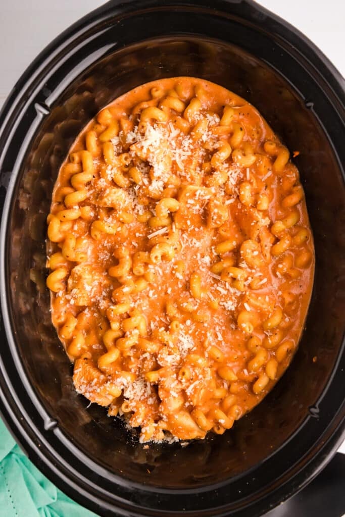 overhead shot of creamy chicken pasta topped with cheese in a slow cooker.