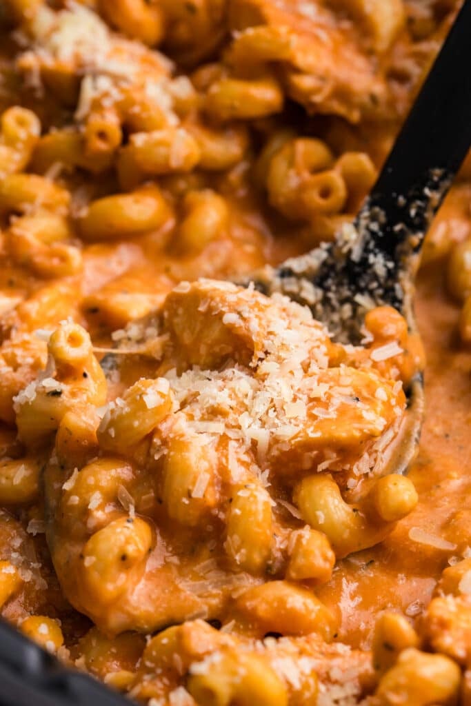 spoon scooping creamy chicken pasta from a slow cooker.