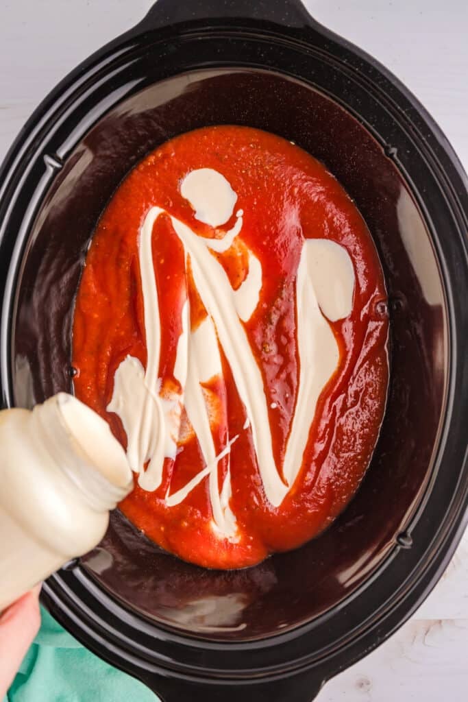 alfredo sauce pouring into marinara in a crockpot.