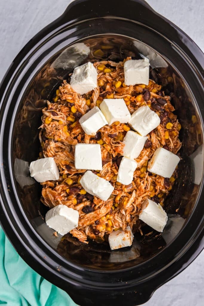 cubed cream cheese on shredded chicken in a crockpot.