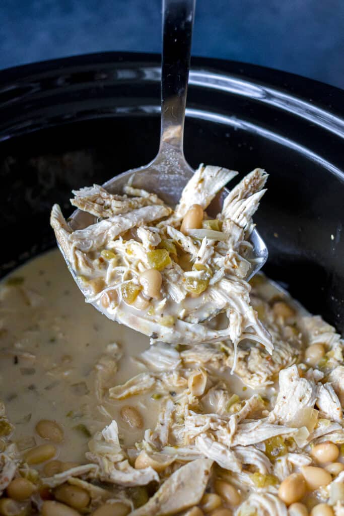 ladle lifting a scoop of white chicken chili from a slow cooker.