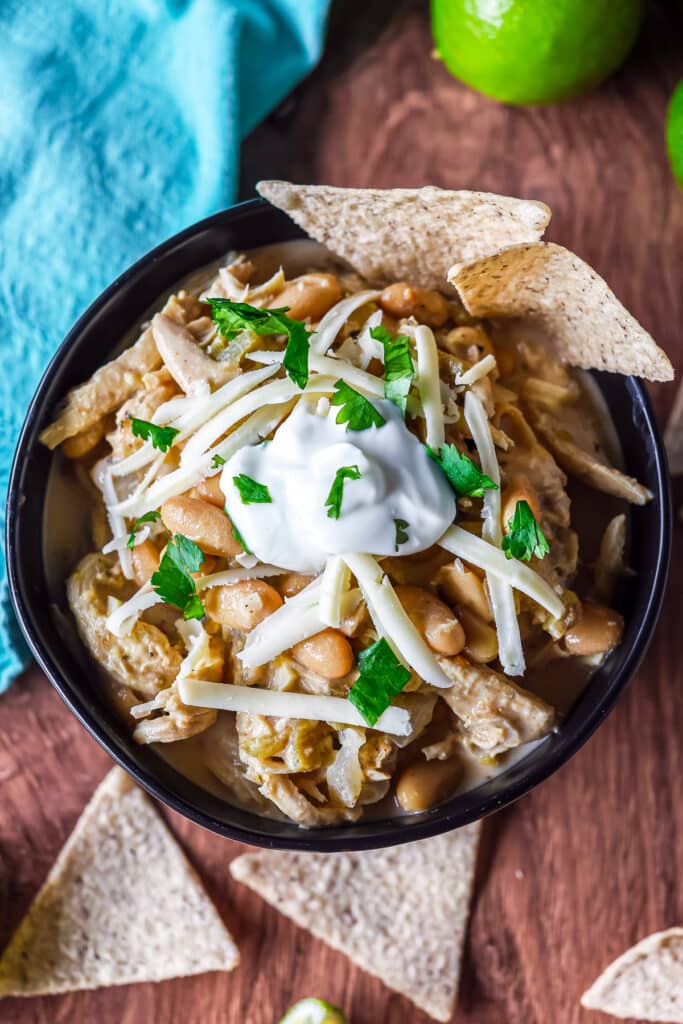 overhead shot of a bowl of white chicken chili topped with sour cream, cheese, and tortilla chips.