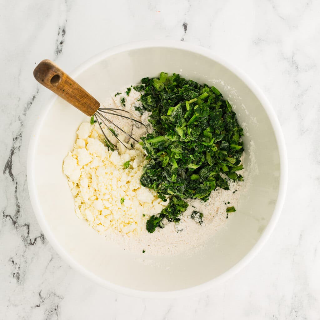 overhead shot of frozen spinach and flour in a mixing bowl.