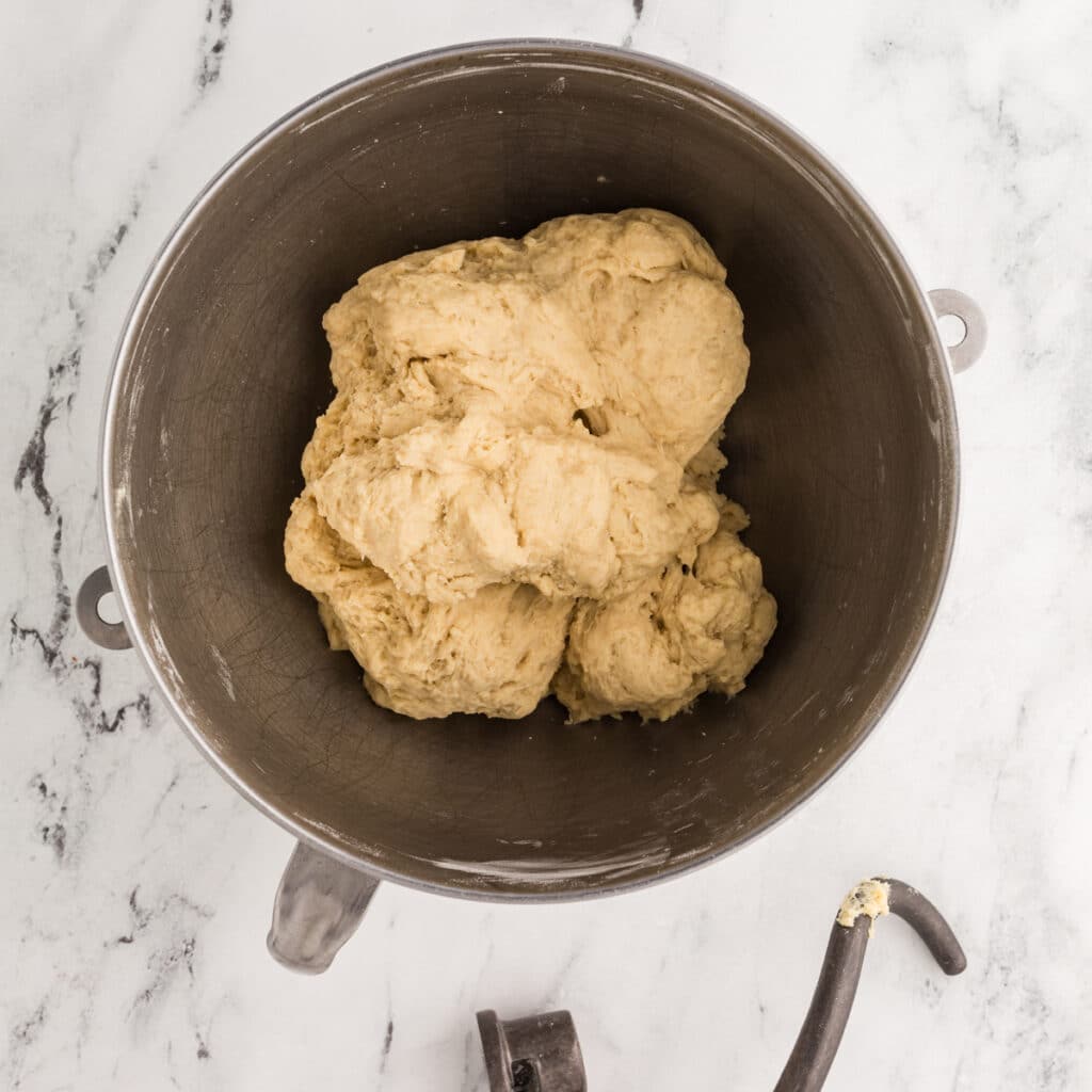 dough in a mixing bowl next to a dough hook.
