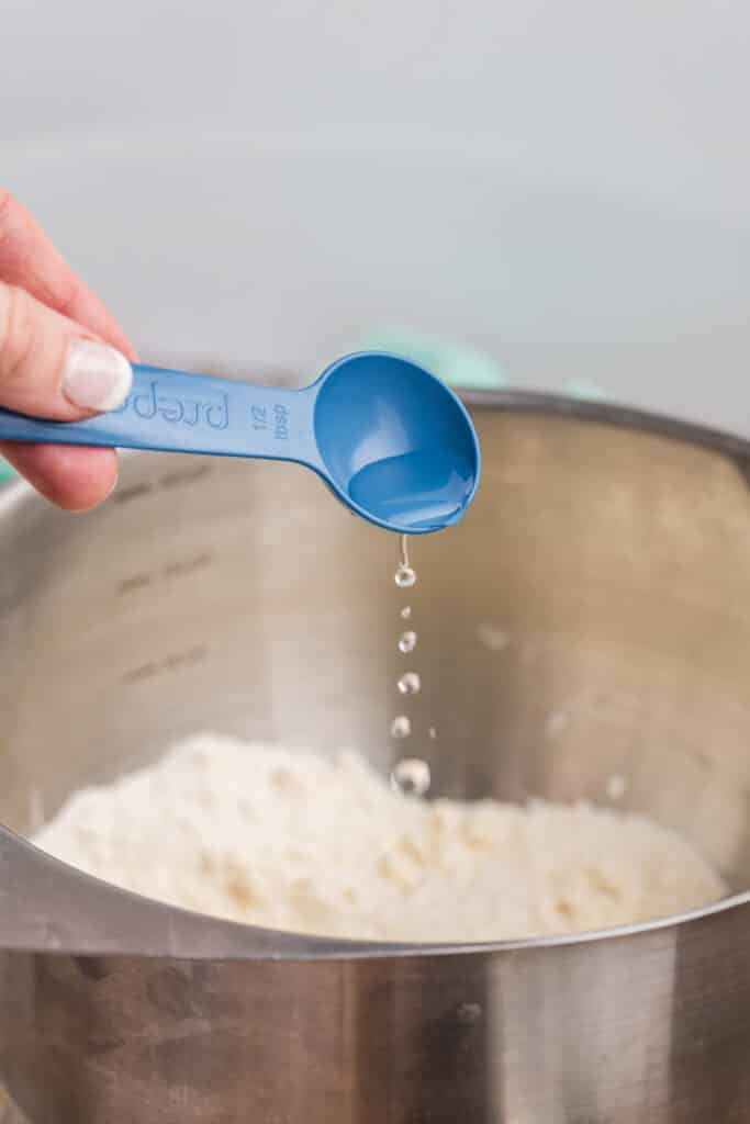 a measuring spoon drizzling water into a bowl.