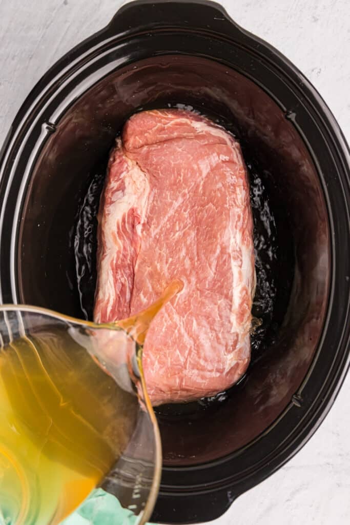 broth pouring on a pork loin a crockpot.