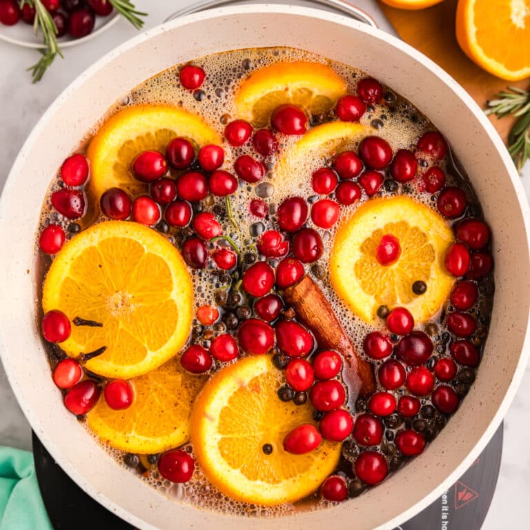 A pot with orange slices, cranberries, rosemary, and cinnamon sticks in liquid.
