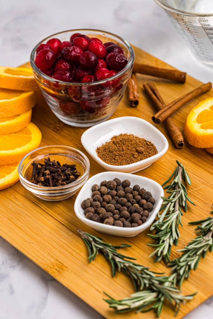 Ingredients for a simmer pot, including oranges, cranberries, cinnamon, and spices on a wooden board.