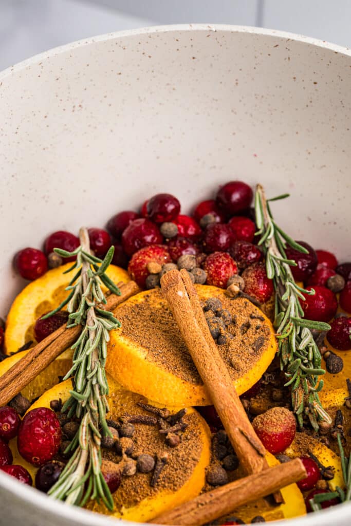 A pot filled with sliced oranges, cranberries, cinnamon sticks, rosemary sprigs, and spices.