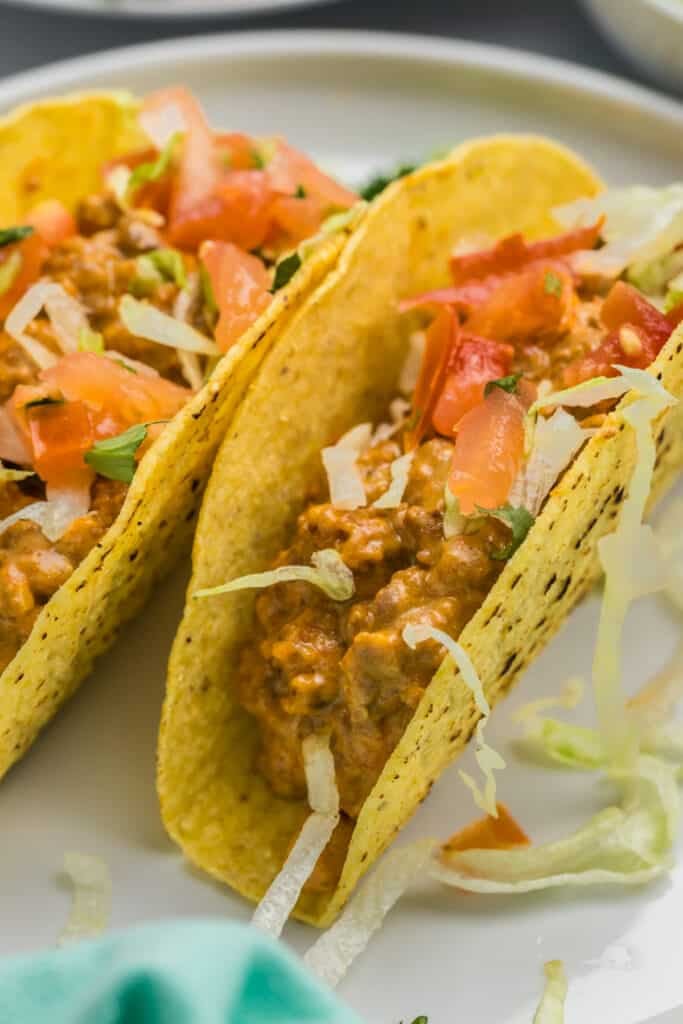 two crunchy tacos topped with tomatoes and lettuce.