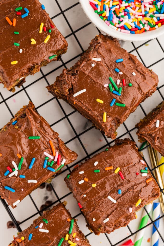 overhead shot of slices of confetti snack cake with chocolate frosting and sprinkles on a cooling rack.