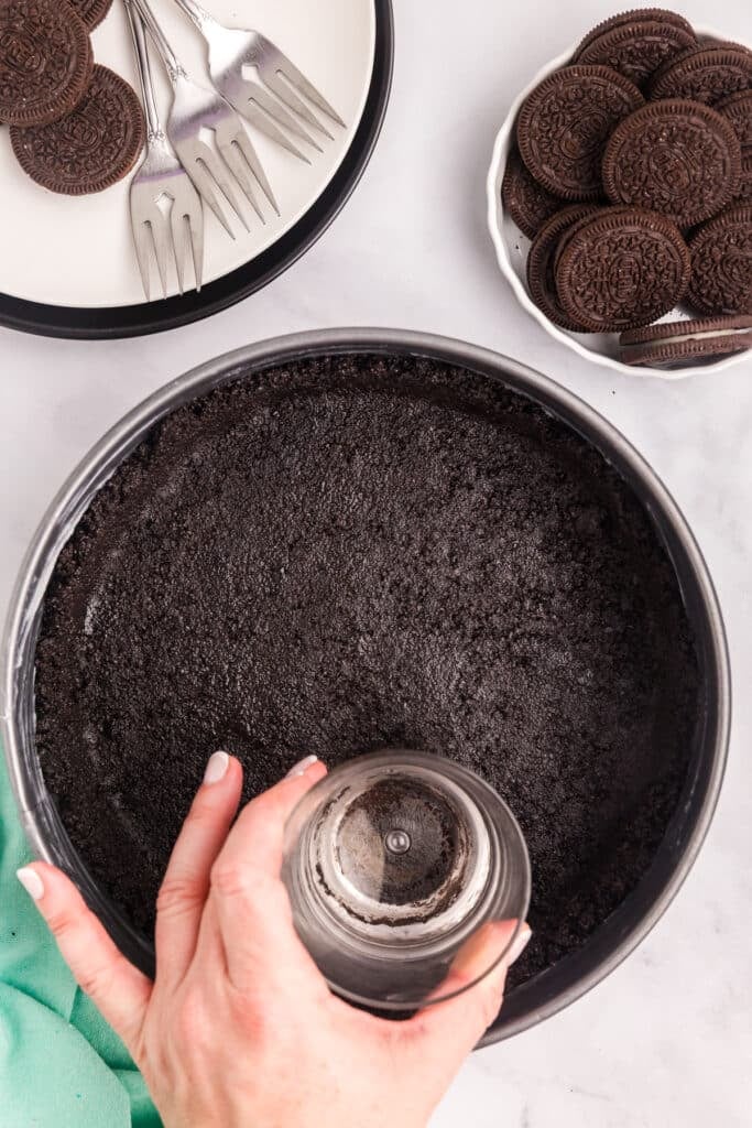 Pressing cookie crumbs into a pan for a cheesecake crust.