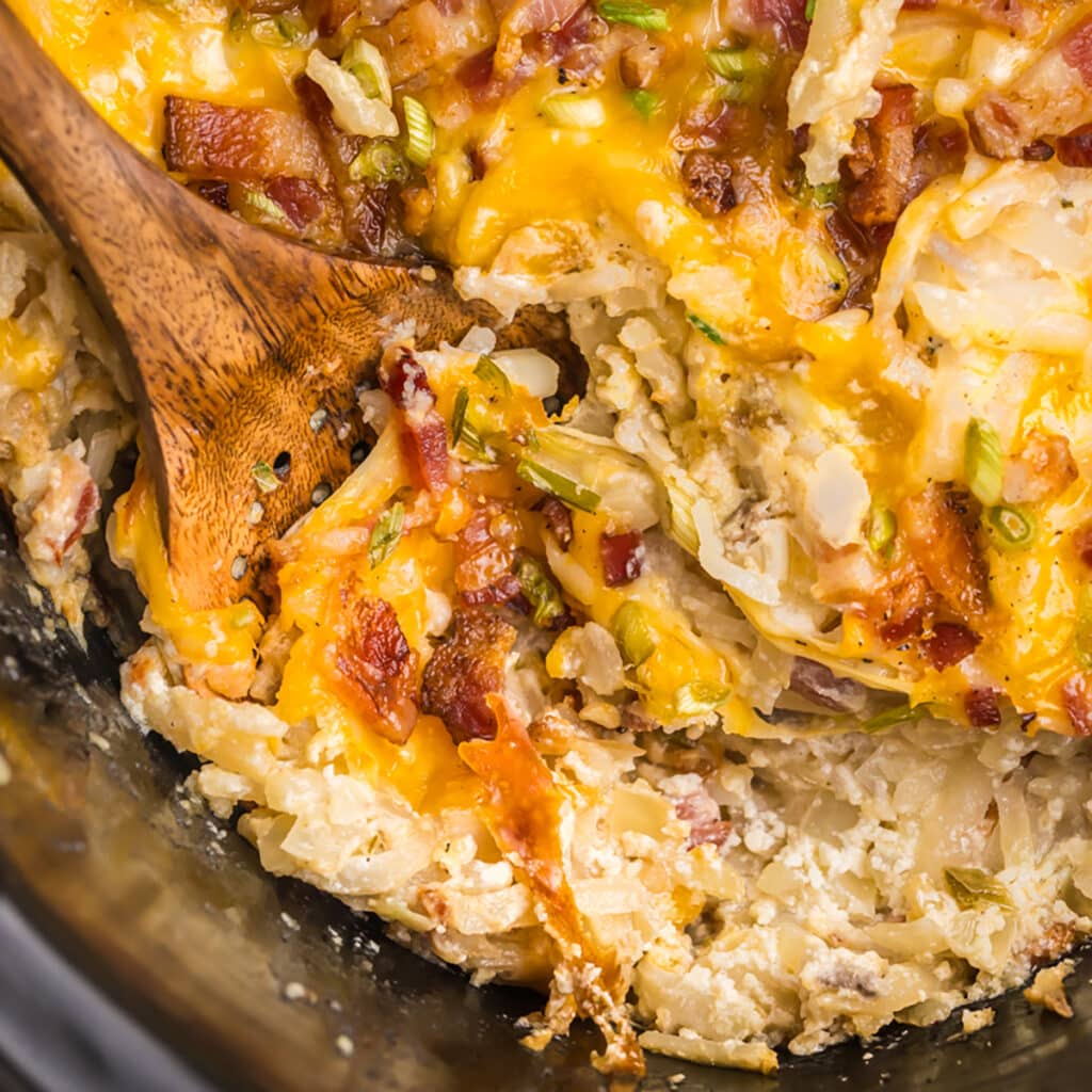 A close-up of cheesy hash brown casserole with bacon and scallions.