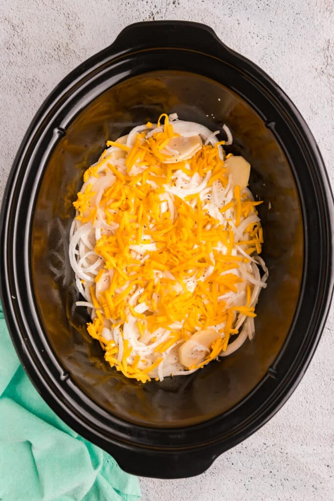 Uncooked scalloped potatoes topped with shredded cheese in a crockpot.