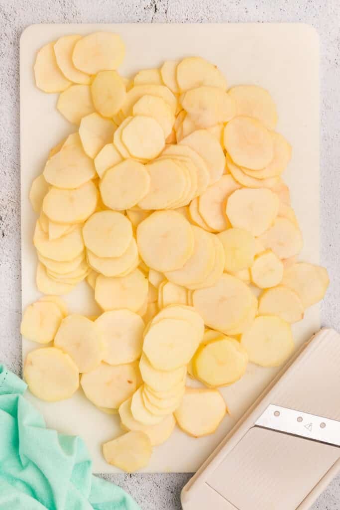 thinly sliced potatoes next to a mandoline.
