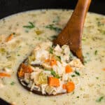 Close-up of a wooden ladle lifting a portion of creamy turkey and rice soup, showing chunks of turkey, diced carrots, celery, and parsley in a creamy broth.