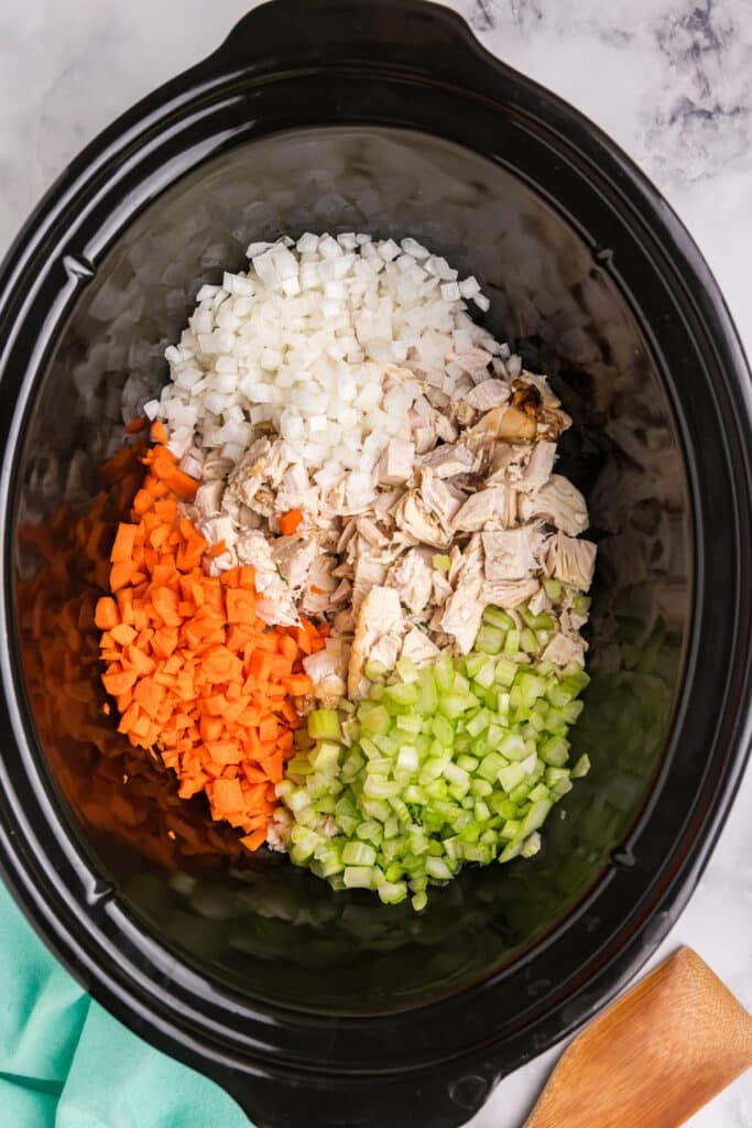 overhead shot of diced carrots, onion, celery, and turkey in a crockpot.